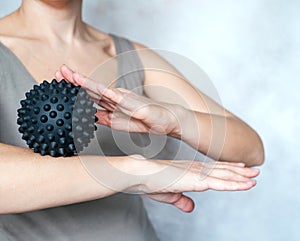 A young woman massages her elbow with a spiky trigger point ball, tennis elbow exercises