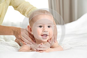 Young woman massaging cute little baby on bed
