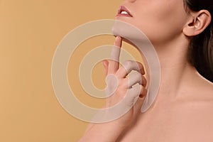 Young woman massaging her face on beige background, closeup. Space for text