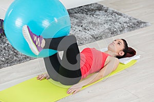 young woman on mat holding fitness ball with legs