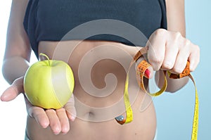 Young woman measuring body holding apple