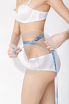 Young woman measuring her perfect slim body iwith measuring tape over white background