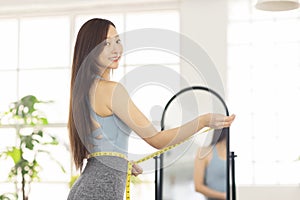 Young woman measuring waist with tape  in front of mirror.Weight loss concept