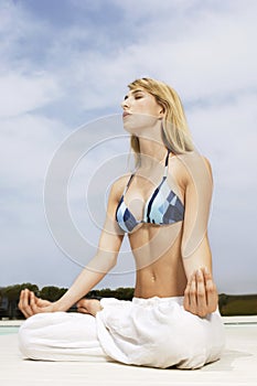 Young Woman Mediating In Lotus Position At Poolside