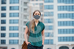 A young woman in a medical face mask thrusting hands into pockets of trousers