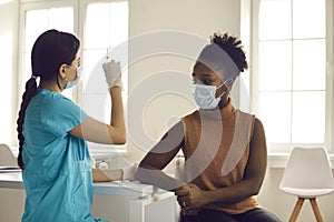 Young woman in medical face mask waiting for nurse to get syringe ready for injection