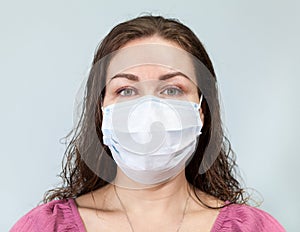 Young woman in medical face protection mask on blue background, looking at camera