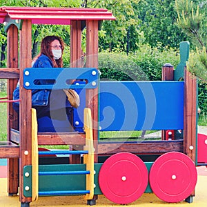 Young woman in a medical mask on a children playground in a toy train