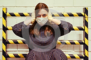 A young woman in a medical mask covered her ears against a black-and-yellow barrier. Siren and sound warning of problems