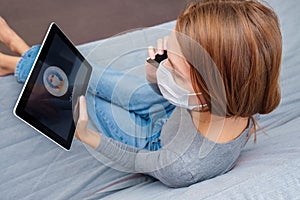 A young woman in a medical mask sits at home in quarantine and calls an online doctor for advice on the symptoms of coronavirus