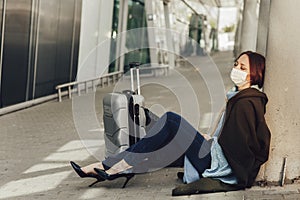 Young woman in medical mask sits near luggage in airport. Tortured by the flight, the woman dozes off