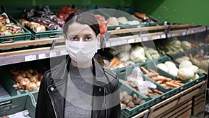 Young woman in medical mask stands in supermarket. Protection from coronavirus, purchase of food for quarantine. Defecit of