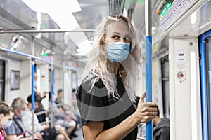 Young woman in a medical mask in a subway car. Blonde with long hair in a black T-shirt. Precautions during the coronavirus