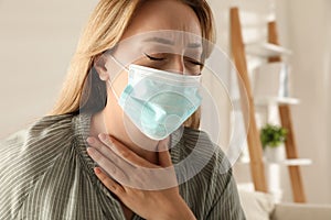 Young woman in medical mask suffering from pain during breathing indoors