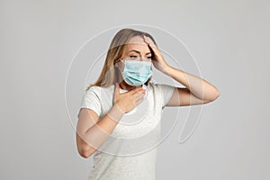 Young woman in medical mask suffering from pain during breathing on light grey background