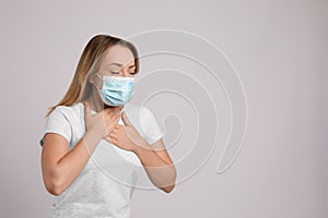 Young woman in medical mask suffering from pain during breathing on light grey background, space for text