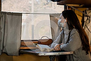 A young woman in medical mask is traveling by train alone. Taking precautions