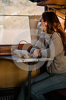 A young woman in medical mask is traveling by train alone. Taking precautions