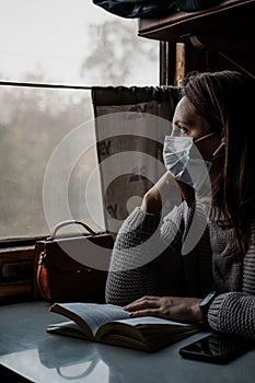 A young woman in medical mask is traveling by train alone. Taking precautions