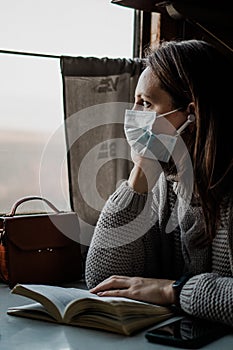 A young woman in medical mask is traveling by train during coronavirus pandemic