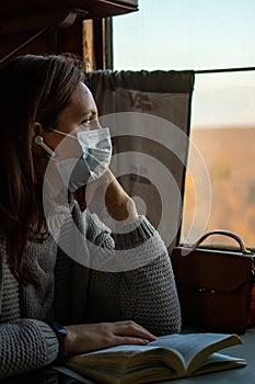 A young woman in medical mask is traveling by train during coronavirus pandemic