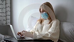 Young woman in medical mask working from home with laptop