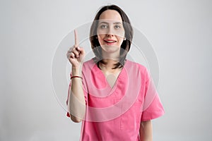 Young woman medical professional nurse or doctor dressed with pink hospital clothes with her finger up has come up with an idea