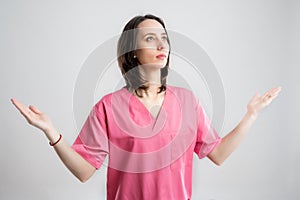 Young woman medical professional nurse or doctor dressed with pink hospital clothes with open arms looking up, side view
