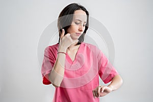 Young woman medical professional nurse or doctor dressed with pink hospital clothes showing call me gesture and looking her watch