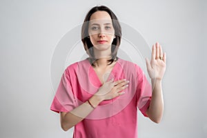 Young woman medical professional nurse or doctor dressed with pink hospital clothes showing oath