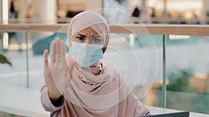 Young woman in medical protective mask shows with palm stop sign gesture forbidding to approach due to pandemic outbreak