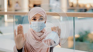 Young woman in medical protective mask shows with palm stop sign gesture forbidding to approach due to pandemic outbreak