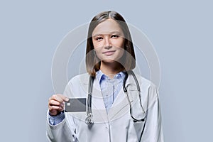 Young woman medical specialist, doctor holding bank credit card on gray background