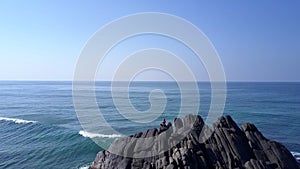 Young woman meditates on cliff against ocean under blue sky