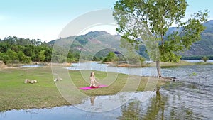 Young woman meditates on mat against green landscape