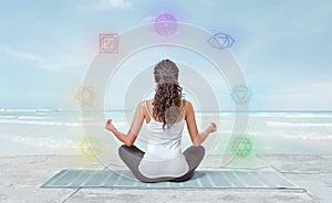 Young woman is meditating on the beach with chakras glowing around her