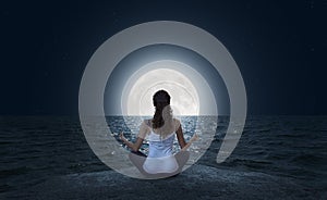 Young woman meditating on the beach at full moon photo