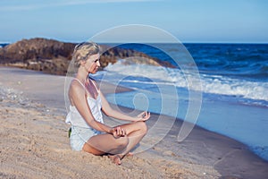 Young woman meditating on beach, pier in lotus position at sunrise