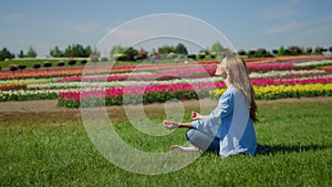Young woman meditating on green grass. Hipster girl sitting in lotos outdoors.