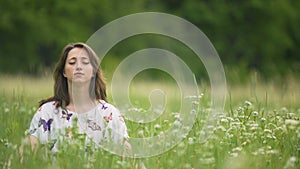 Young woman meditating in high green grass, oneness with nature, stop thinking