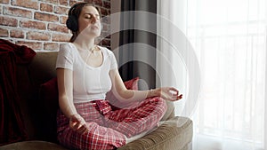 Young woman meditating and listening to relaxing music in headphones. Concept of relaxation, healthy lifestyle, resting at home