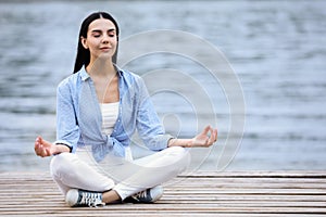 Young woman meditating near river. Space for text