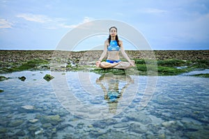 Young woman, meditating, practicing yoga and pranayama at the beach. Sunset yoga practice. Hands in gyan mudra. Water reflection.