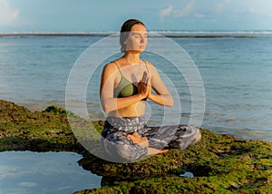 Young woman, meditating, practicing yoga and pranayama at the beach. Sunset yoga practice. Hands in namaste mudra, closed eyes.