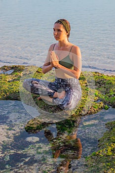 Young woman, meditating, practicing yoga and pranayama at the beach. Sunset yoga practice. Hands in namaste mudra. Melasti beach,