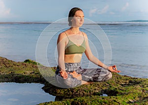 Young woman, meditating, practicing yoga and pranayama at the beach. Sunset yoga practice. Lotus pose. Hands in gyan mudra.