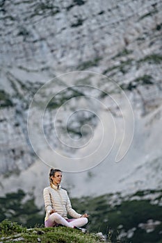 Young woman meditating on a rock in high mountains