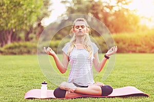 Young woman meditating on yoga mat in park at sunset