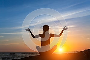 Young woman meditation on the ocean during amazing sunset.