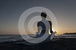 Young woman meditation in a yoga pose at the beach on sunset